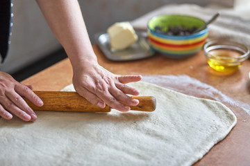 Women's hands roll the dough on the kitchen table. Women's hands with rolling pin