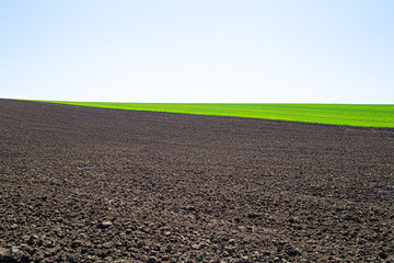 Beautiful black earth fields in Ukraine. Agricultural rural landscape, colorful hills. Plowed dark land and green fields.