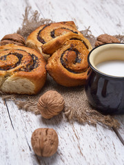 Basket of homemade buns with jam, served on old wooden table with walnuts and cup of milk