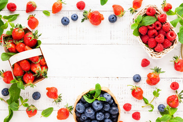 Various fresh berries in basket on white wooden background, top view. Concept of summer food. Flat lay, copy space.