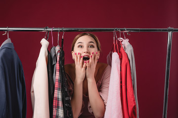 Beautiful girl chooses and tries on clothes on a red background. The concept of choosing and buying clothes, shopaholism and consumerism