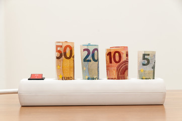 Euro banknotes inserted into an extension socket on a wooden surface. Expensive concepts of energy...