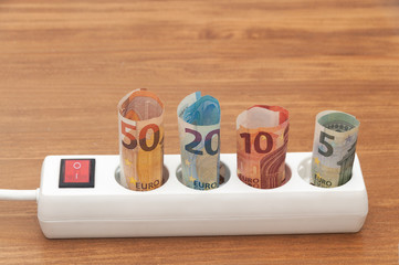 Euro banknotes inserted into an extension socket on a wooden surface. Expensive concepts of energy and cost of electricity. Front view.