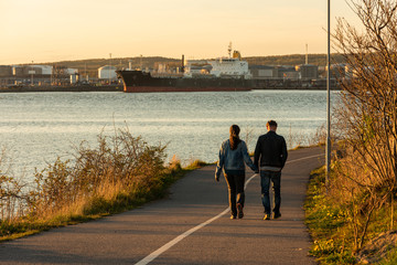 Couple walking on a combined bicycle and walking path at sunset by a harbour..