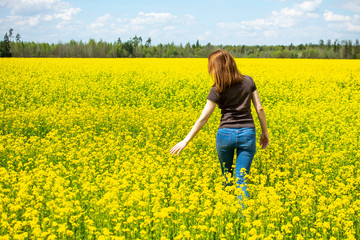 A young woman walks through a yellow-blooming rapeseed field.