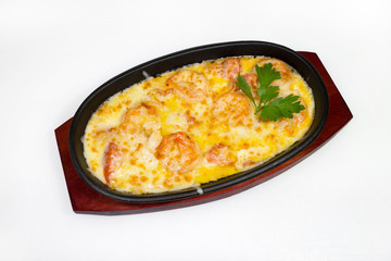 Casserole with fish, shrimp and other seafood in an oval black roasting pan on a plate on a white background
