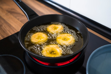 Close up of a woman frying homemade donuts in her kitchen following an online recipe.