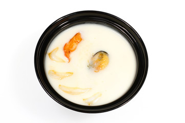 Puree milk soup with shrimps and mussels in a black deep plate on a white background