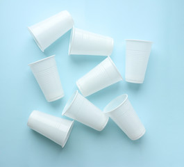 A lot of white disposable plastic cups are lying on a blue background. Selective focus. Background of plastic cups. Harmful plastic.