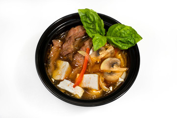 Beef soup with mushrooms, cheese and vegetables in a black deep plate on a white background