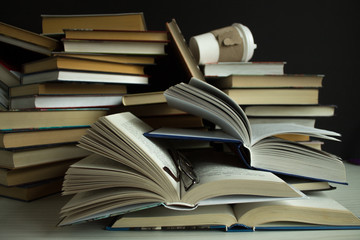 Clutter on the table - a lot of open and closed books close-up and a paper Cup of coffee with a lid