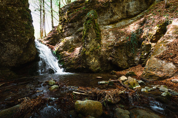Beautiful view of moody and dramatic waterfall with big rocks and stones on foreground in forest. Small dark waterfall in European forest flows throught the tunnel of rocks