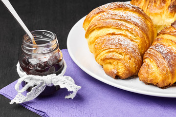 Close up french croissants, jar of jam served on a purple serviette. Homemade baking from puff dough.