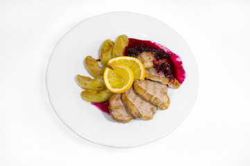 Slices of grilled pork meat poured with blackcurrant sauce, as well as baked apple slices in sweet syrup and garnished with lemon