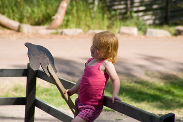 Kleines rothaariges Mädchen wartet mit einem Steckenpferd auf einem Spielplatz im Sommer