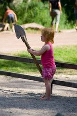 Kleines rothaariges Mädchen mit einem Steckenpferd auf einem Spielplatz im Sommer