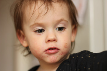 Close-up portrait of a little cute white baby with a dirty face in soft light and blurry background