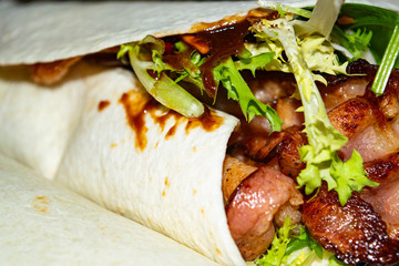 Leafy salad, sliced vegetables, sauce and fried bacon slices wrapped in pita bread. Delicious homemade Shawarma. Close up.