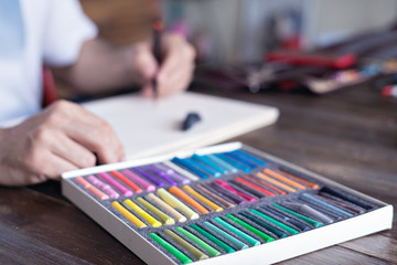 person, artist painting with a pastel crayon chalk on sketchbook on wooden table, selective focus.