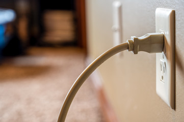 Side view of white power cord plugged into a white wall outlet - obrazy, fototapety, plakaty