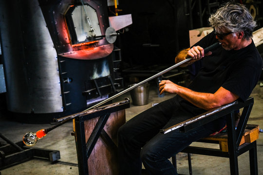 Artist glass blower blowing in his cane the glass paste. A glass crafter is burning and blowing an art piece