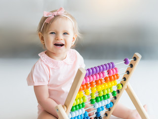 Adorable baby girl with educational toy scores in home or kindergarten