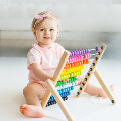 Adorable baby girl with educational toy scores in home or kindergarten