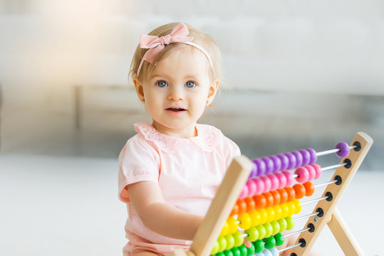 Adorable baby girl with educational toy scores in home or kindergarten