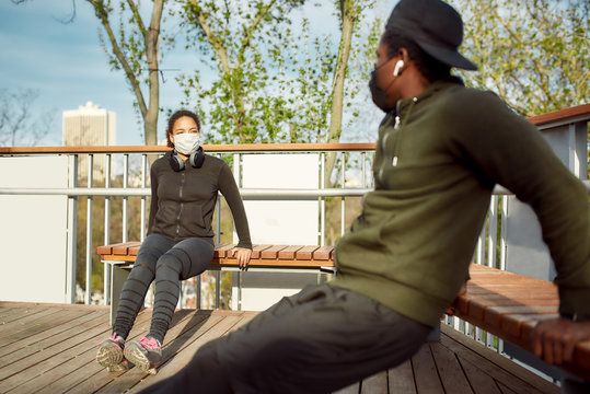 Staying fit during quarantine. Healthy african couple in protective masks working out in park outdoors. Doing push-ups exercises on bench, training triceps