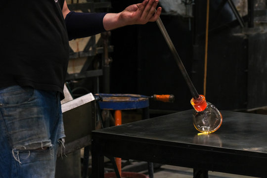 Artist glass blower working glass paste on his workbench. A glass crafter is burning and blowing an art piece