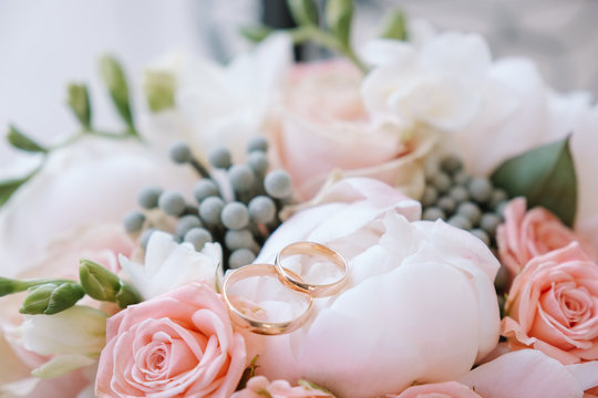 a pair of classic gold wedding rings sits on the bride's bouquet of pink roses