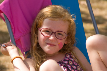 Mädchen mit roten Haaren und Brille sitzt im Sommer auf einem Campingstuhl mit Pflaster im Gesicht