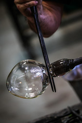 Artist glass blower working glass paste on his workbench. A glass crafter is burning and blowing an art piece