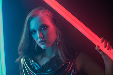 Fototapeta premium Fashion portrait of beautiful woman posing in colorful bright neon uv blue and red lights. Model wearing luxury earrings. Club, disco style