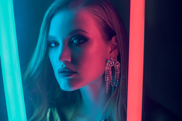 Fashion portrait of beautiful woman posing in colorful bright neon uv blue and red lights. Model wearing luxury earrings