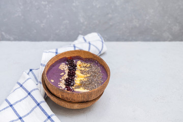 Blackberry smoothie bowl with banana, chia and sunflower seeds in a natural coconut bowl on neutral grey table with space for text