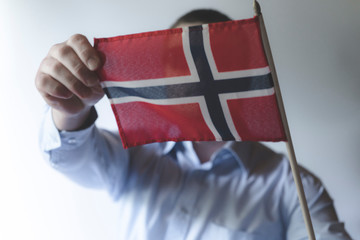 A man in a white blue shirt holding a norwegian flag.