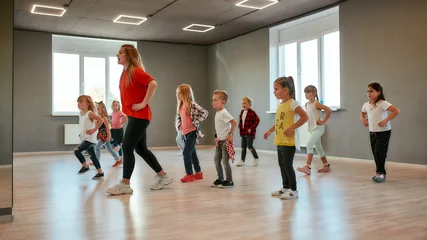 Poster Leren bewegen. Groep kleine jongens en meisjes die dansen terwijl ze choreografieles hebben in de dansstudio. Vrouwelijke dansleraar en kinderen © Svitlana