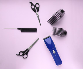 Naklejka premium Layout of hairdressing accessories on a lilac background. Hairdressing scissors, comb and a blue hair clipper with two plastic attachments. Selective focus.