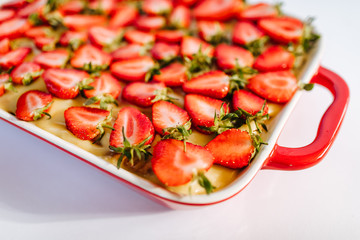 Strawberry cake with in red ceramic baking dish on white background