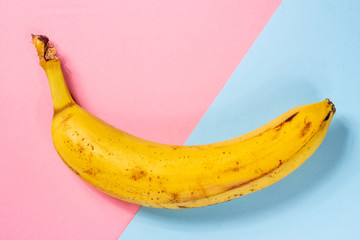 Ugly yellow banana with black spots on a pink and blue background close-up
