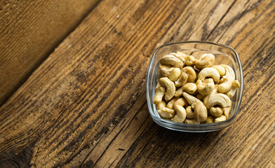 Cashew nuts in a small plate on a vintage wooden table as a background. Cashew nut is a healthy vegetarian protein nutritious food.