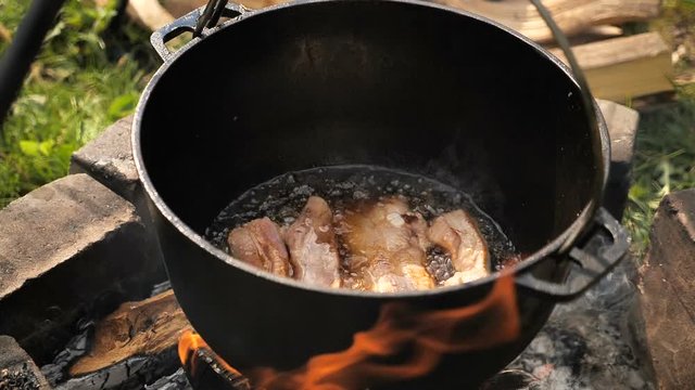 cooking meat in a cauldron on open fire . slow motion