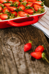 Strawberry cake in baking dish on the old wooden table with white striped towel