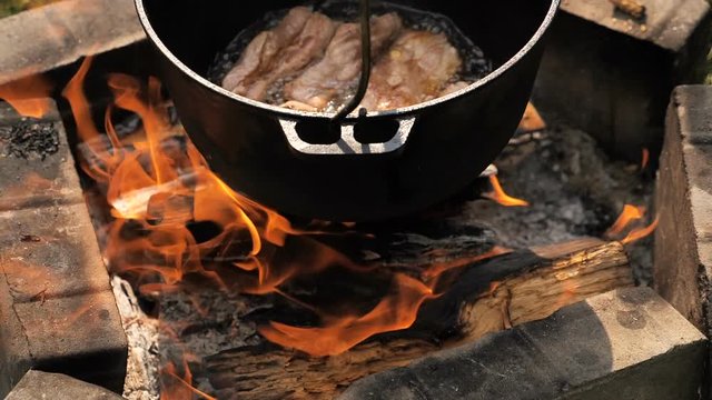 cooking meat in a cauldron on open fire . slow motion