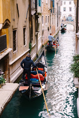 Fototapeta na wymiar Three gondolas with tourists and gondoliers with paddles and in striped sweaters are sailing along a narrow canal between houses in Venice, Italy. Classic entertainment and excursion in the city