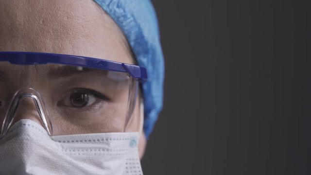 Doctor looking straight to the camera wearing a hat, pollution mask and protection glasses or goglass. Super close up. High quality footage