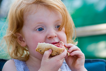 Rothaariges Mädchen isst Brötchen mit Marmelade zum Frühstück