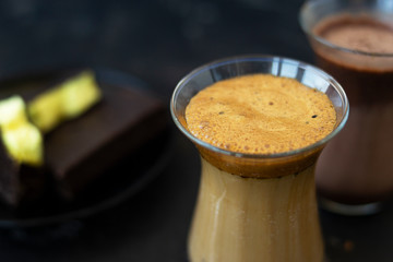 Dalgona coffee and cocoa in glass transparent glasses. Nearby lies a metal spoon with instant coffee, and a chocolate dessert on a saucer