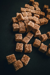 Brown cane sugar in cubes on a black background. Still life. Carbohydrates and non-diet food. Calories.